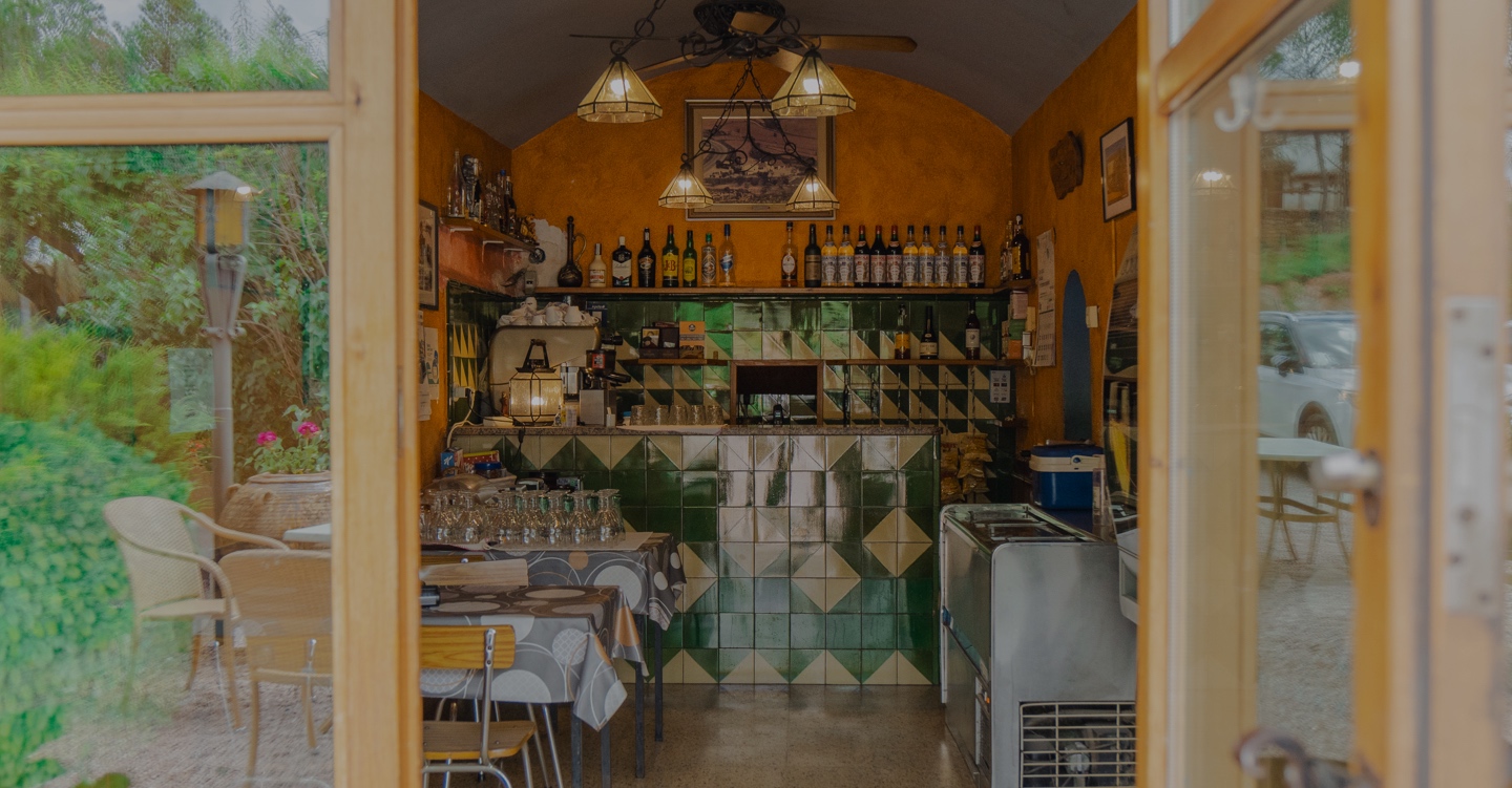 L'interior d'un bar o restaurant tradicional amb una decoració típica. Té unes parets de rajola verda, una barra amb prestatges plens d'ampolles i d'altres elements decoratius, i taules i cadires per als clients.